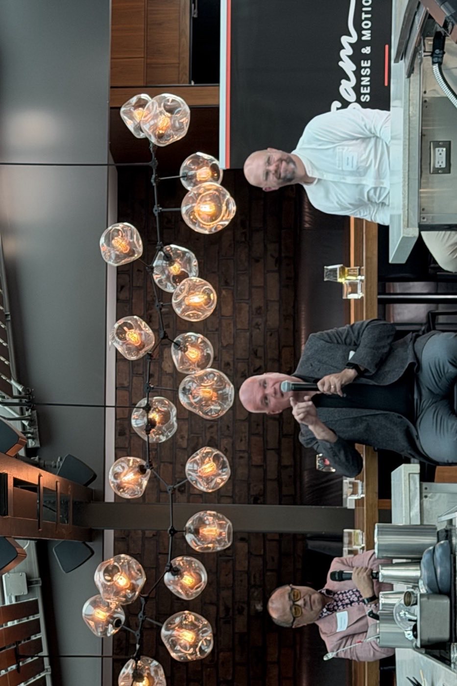 Ben Guanzon, Andr&eacute; Lalande and Tyler Frans seated under the bar&rsquo;s bulb lights, Andr&eacute; speaking into a microphone