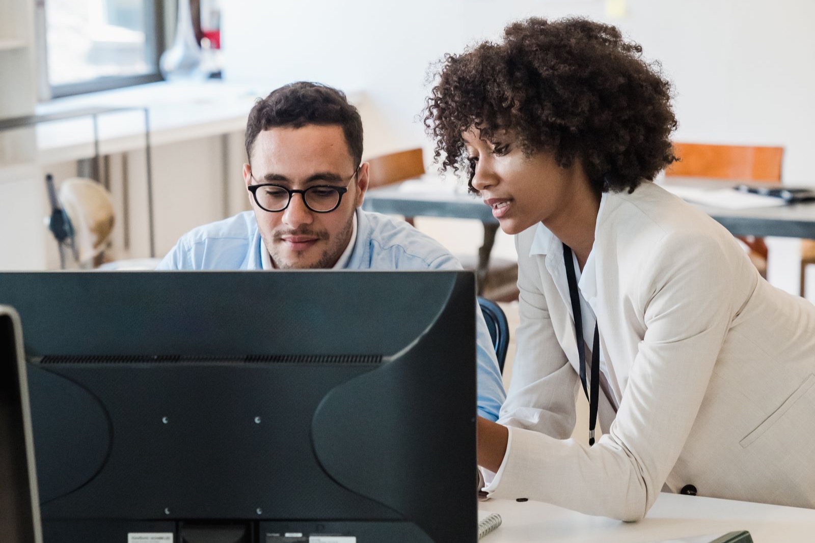 Two colleagues leaning over a computer screen together, talking through what is on it