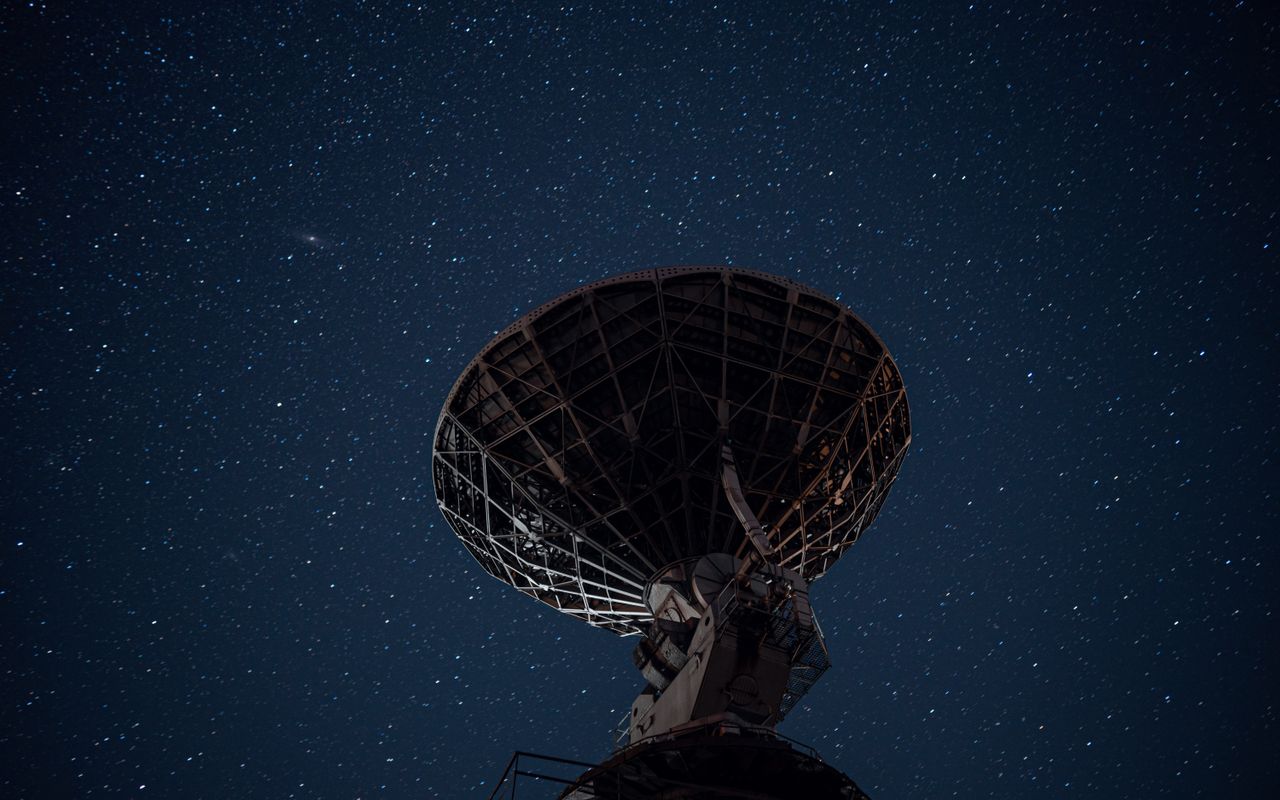 A radio telescope dish under a bright starry night sky