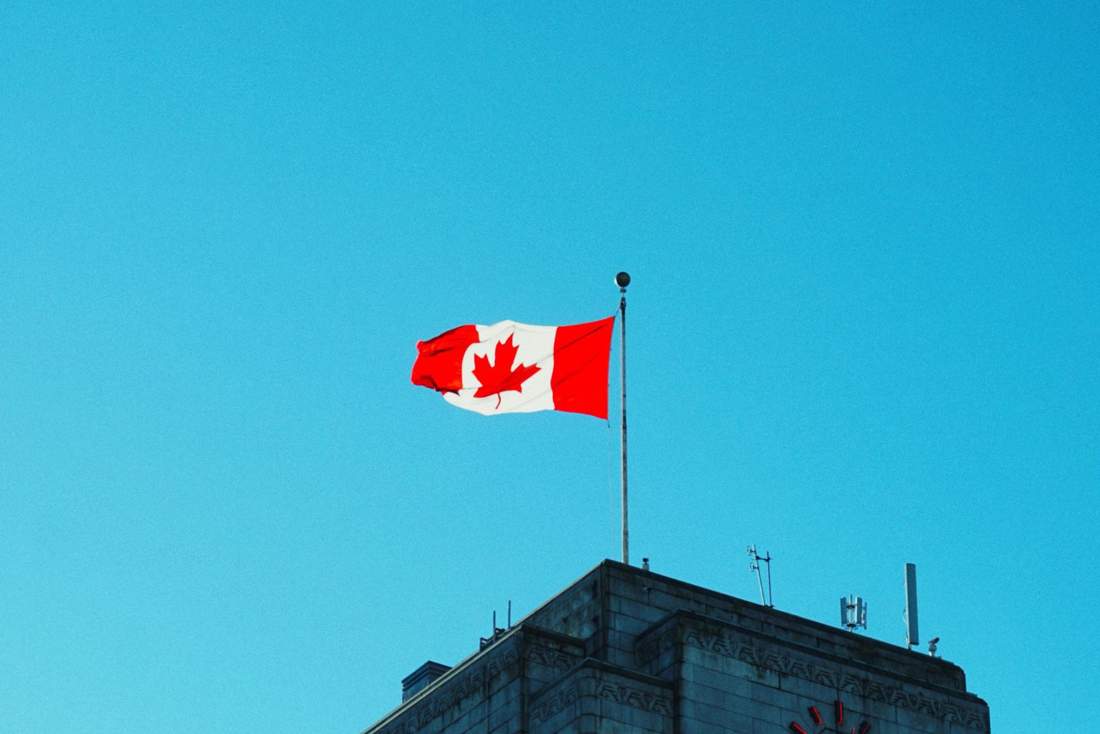 The Canadian flag flying atop Vancouver City Hall against a clear blue sky