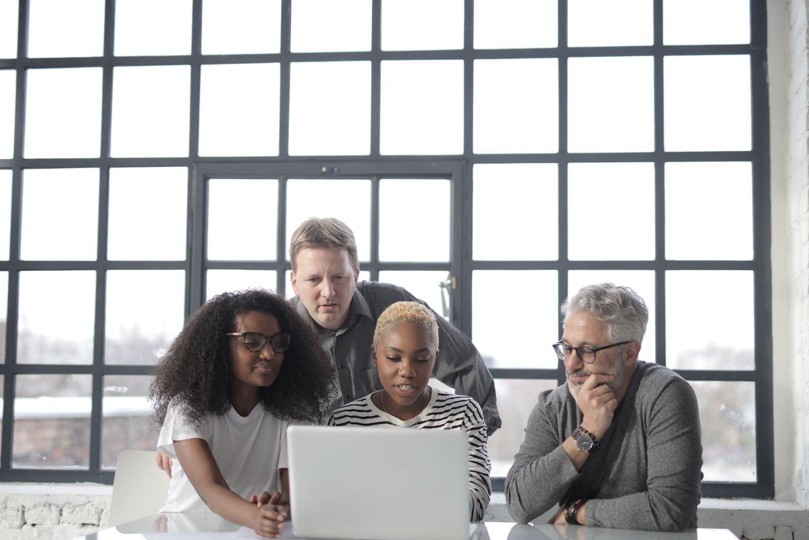 A diverse group of colleagues focused on a laptop together in a modern office