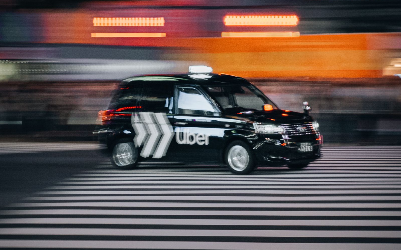 A black Uber taxi speeding across a city crosswalk at night