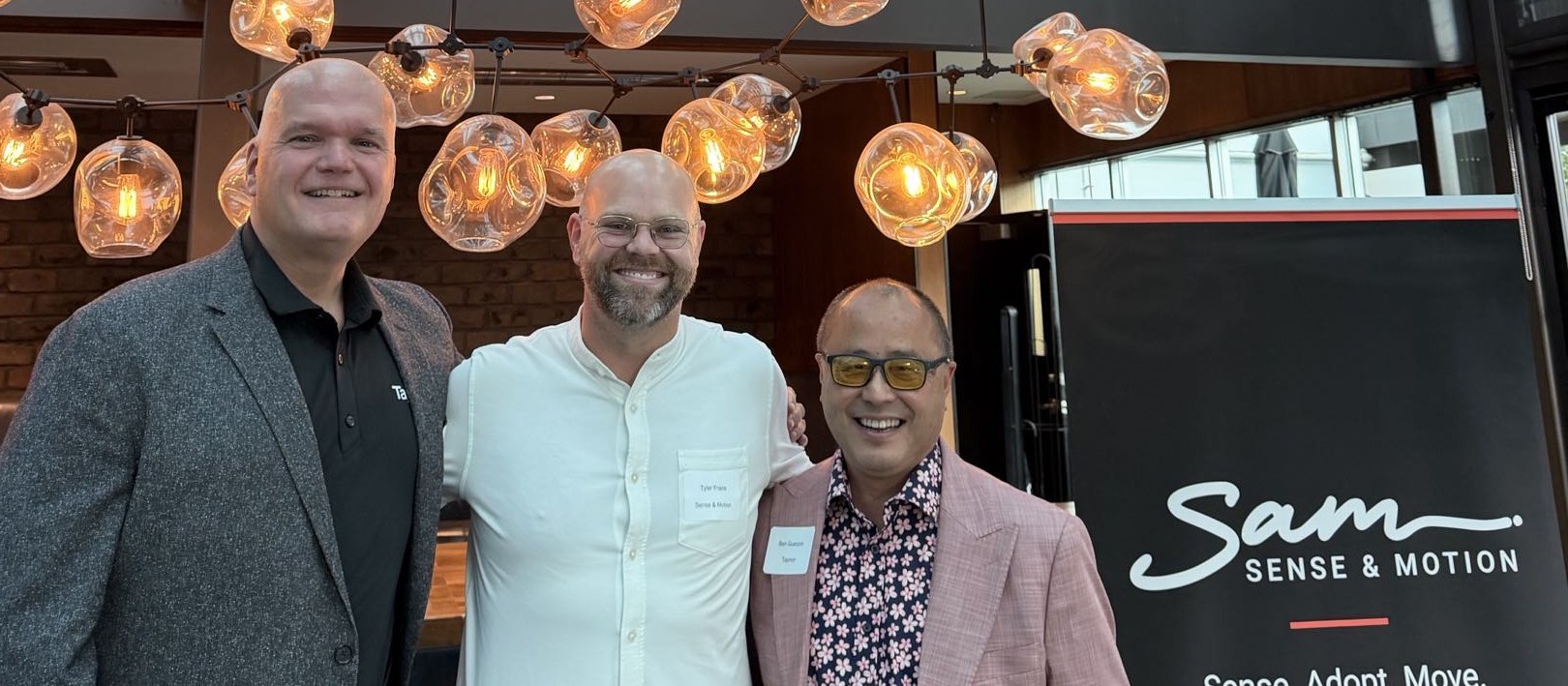 André Lalande, Tyler Frans, and Ben Guanzon standing together beside a Sense & Motion banner at the Happy Hour Conversation in Burnaby