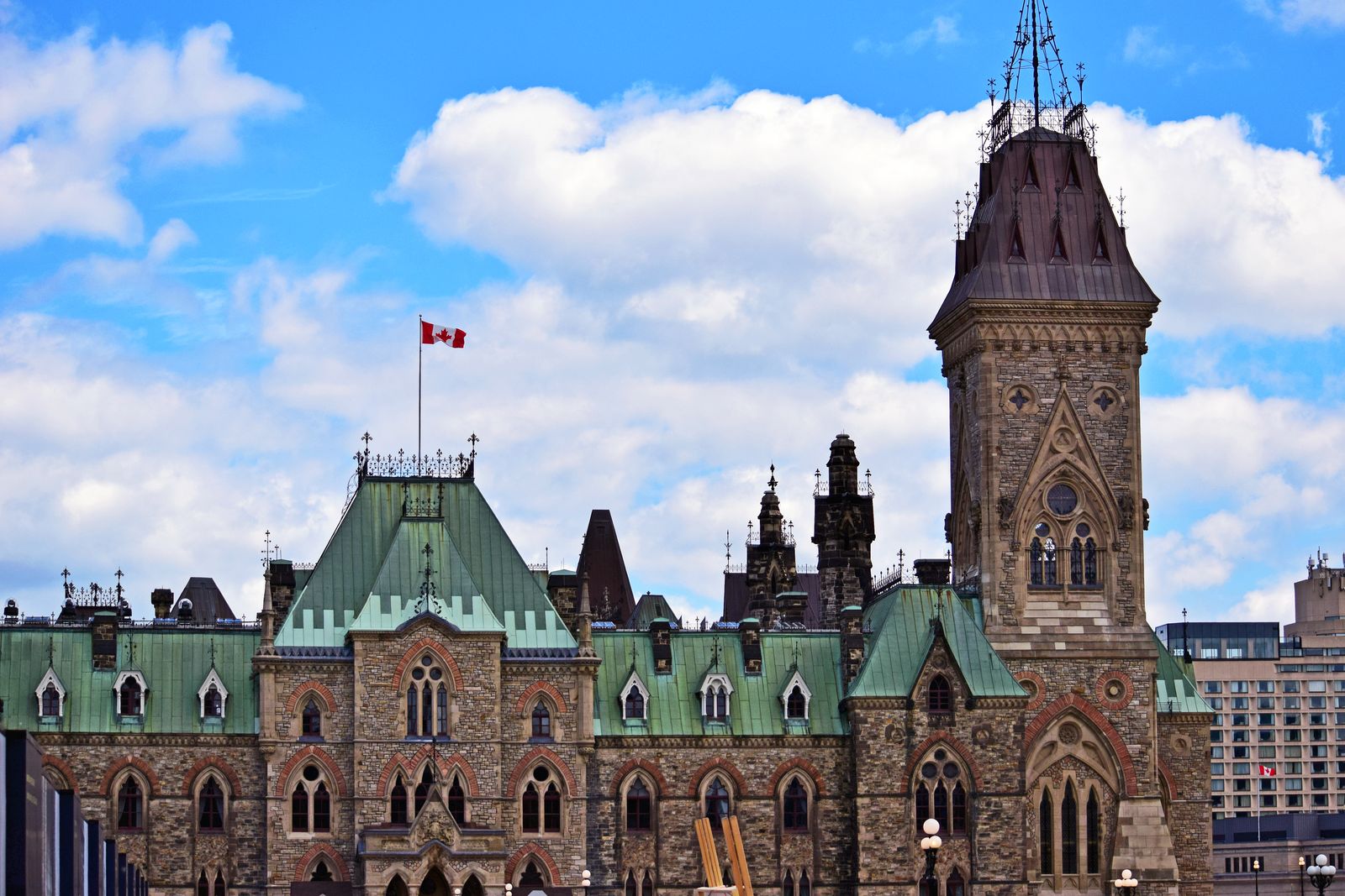 The Centre Block on Parliament Hill in Ottawa under a blue sky with a Canadian flag