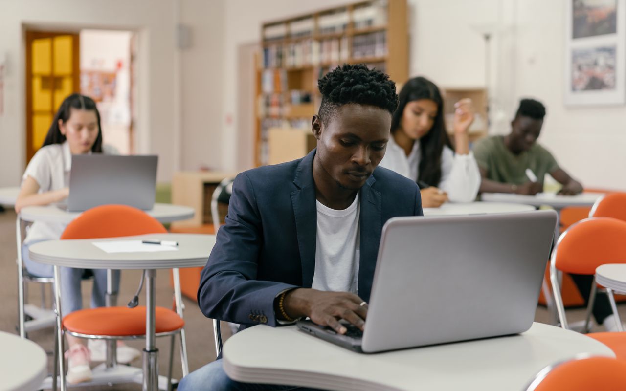 Students working on laptops at desks in a bright library classroom